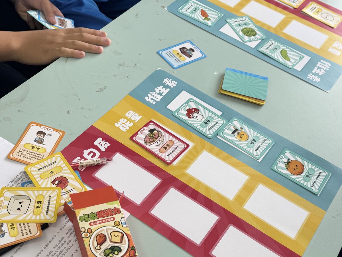 Overhead view of a NutriEmpower game in progress, with a colourful meal board and food cards